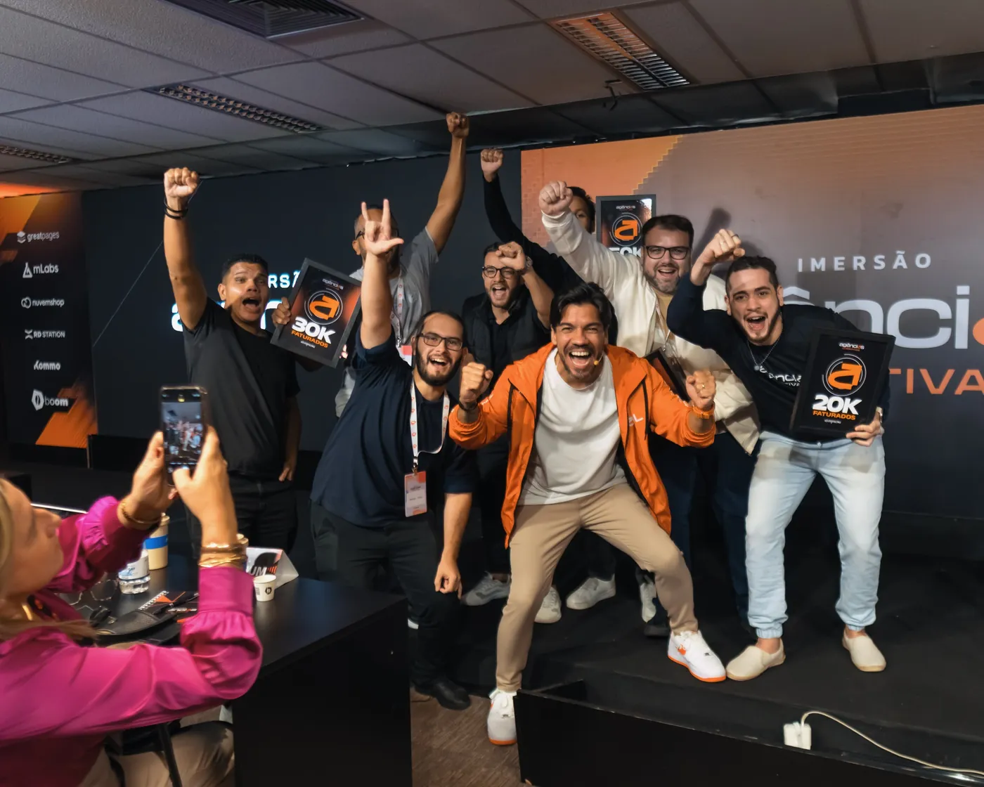 Participantes comemorando no palco com as placas de faturamento